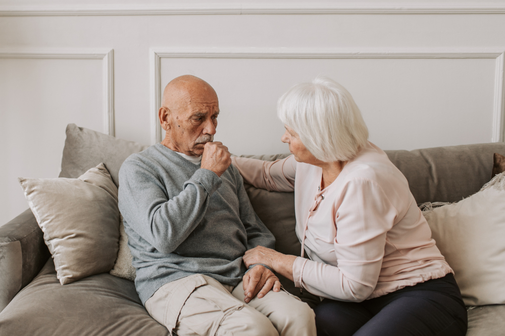 Older man coughing sat next to older woman on sofa