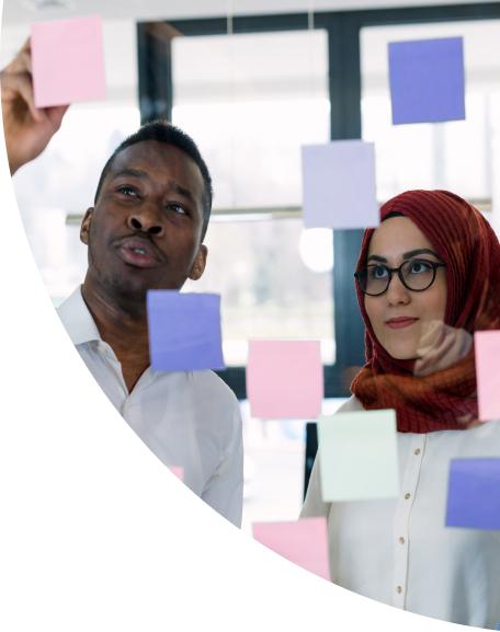 Two people looking at postit notes on a glass wall