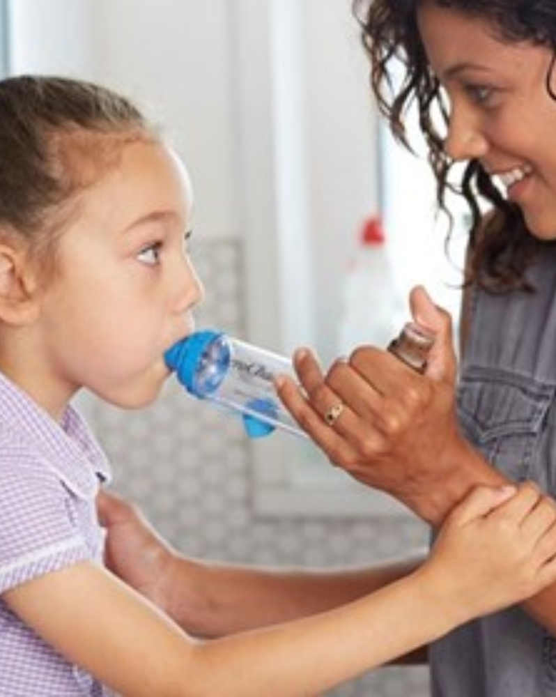 Child using spacer and brown preventer inhaler with help from adult