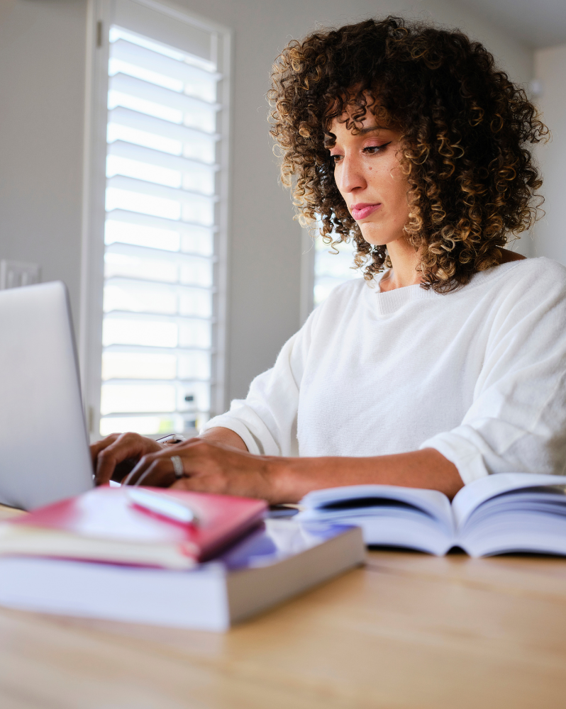 Woman typing on a laptop surrounded by books