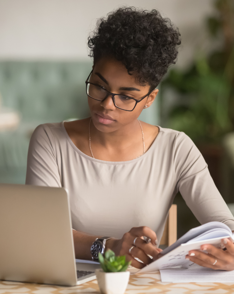 Woman writing notes on a pad while watching laptop screen