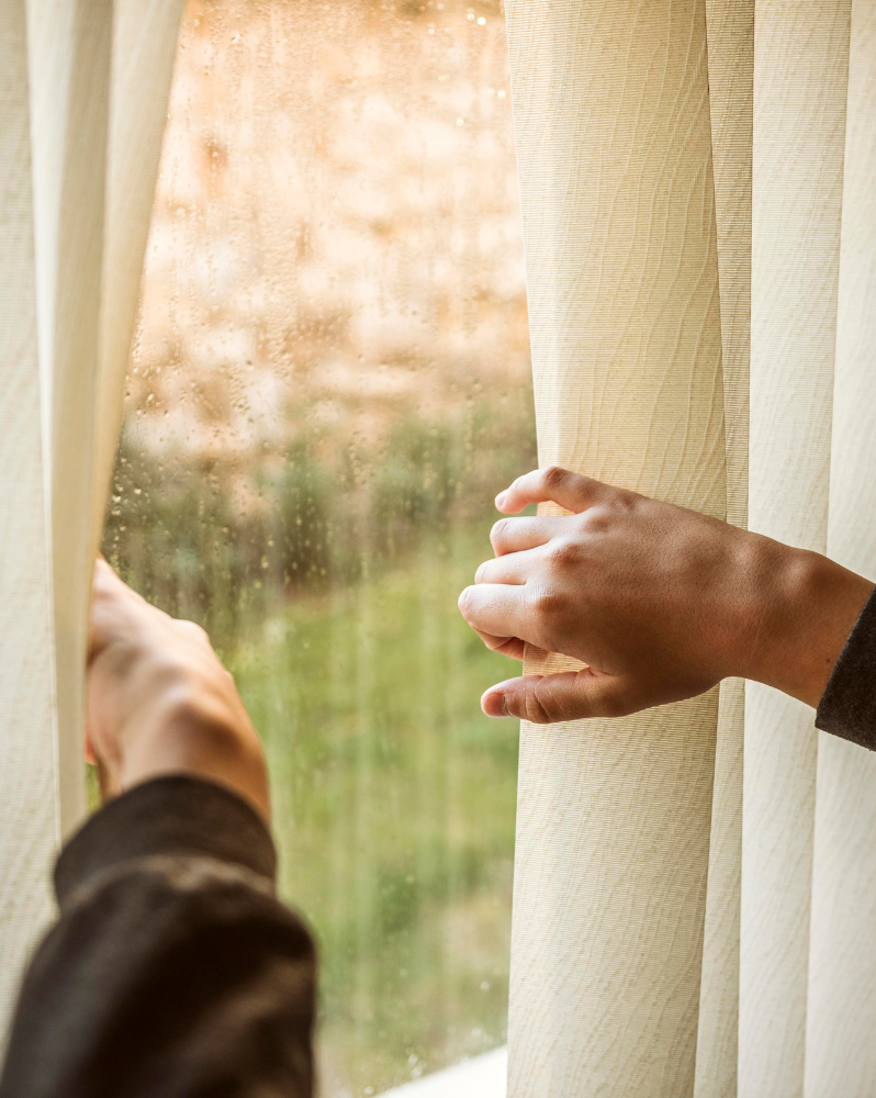 Hands moving blinds aside in rainy window