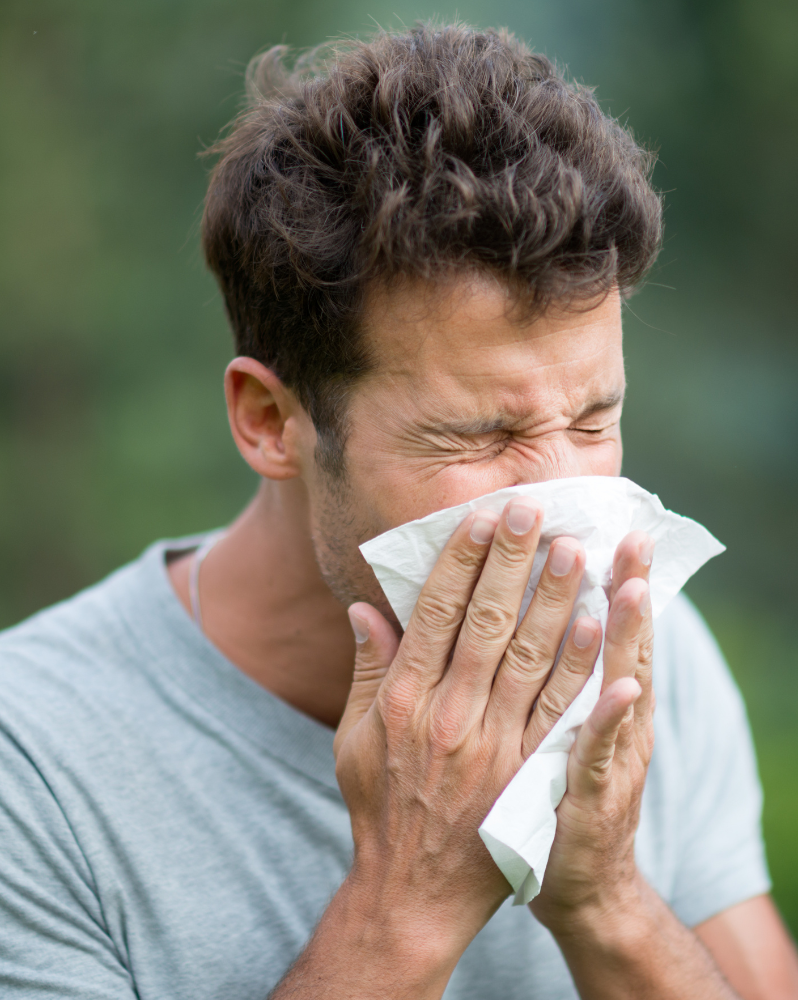 Man sneezing into tissue outdoors