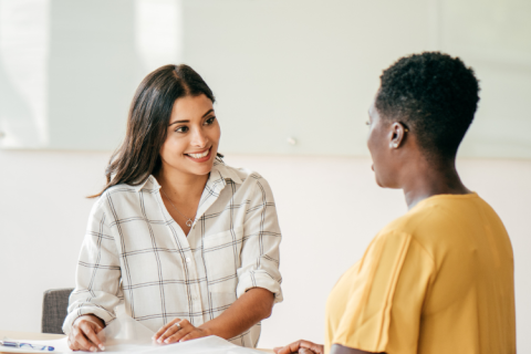 Two women at a table smiling mid interview